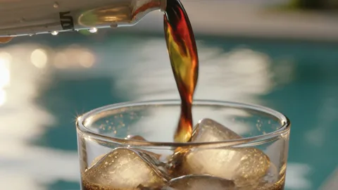 Cold brew pouring from a can into a tumbler of ice, foam building at the rim